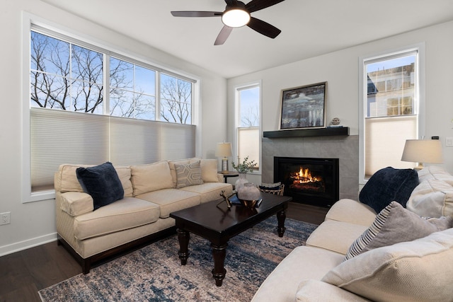 living area with a tiled fireplace, wood finished floors, a ceiling fan, and baseboards