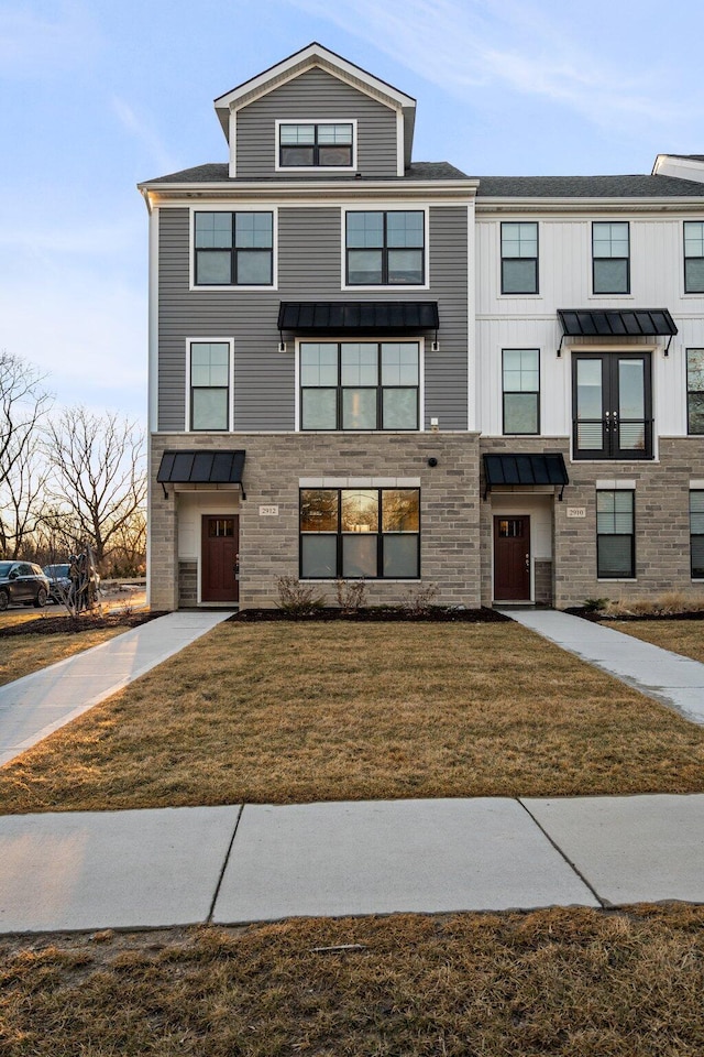 multi unit property with a standing seam roof, stone siding, a front lawn, and metal roof