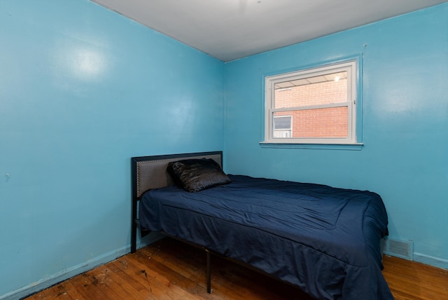 bedroom with baseboards, visible vents, and wood finished floors