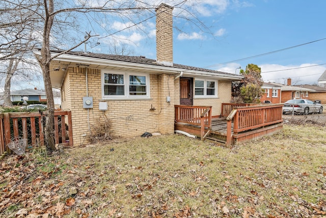 rear view of property featuring brick siding, fence, a yard, a wooden deck, and a chimney