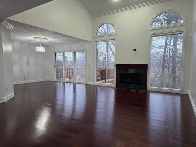 unfurnished living room with baseboards, a towering ceiling, dark wood-style flooring, crown molding, and a fireplace