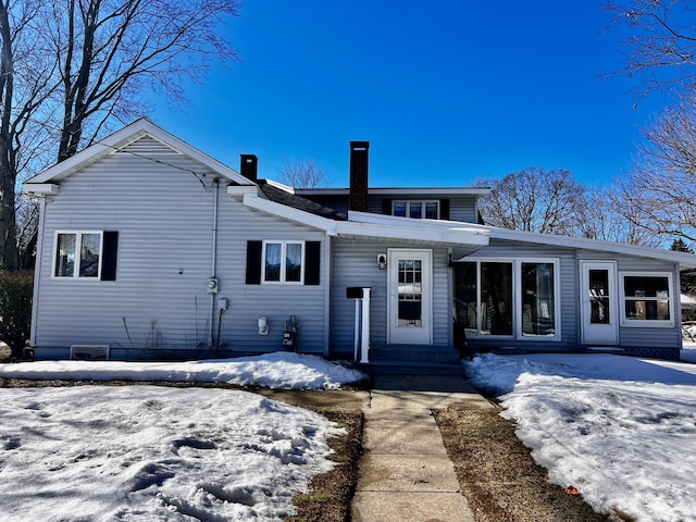 snow covered back of property featuring entry steps and a chimney