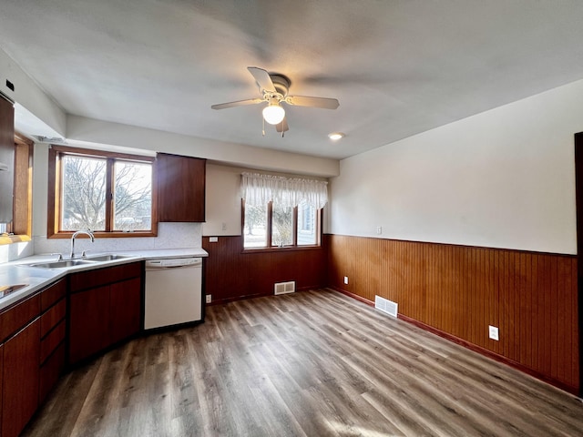 kitchen with white dishwasher, a sink, visible vents, light countertops, and wainscoting