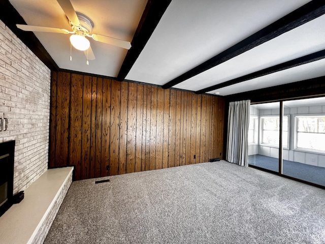 unfurnished living room with beam ceiling, a fireplace, carpet flooring, wooden walls, and brick wall