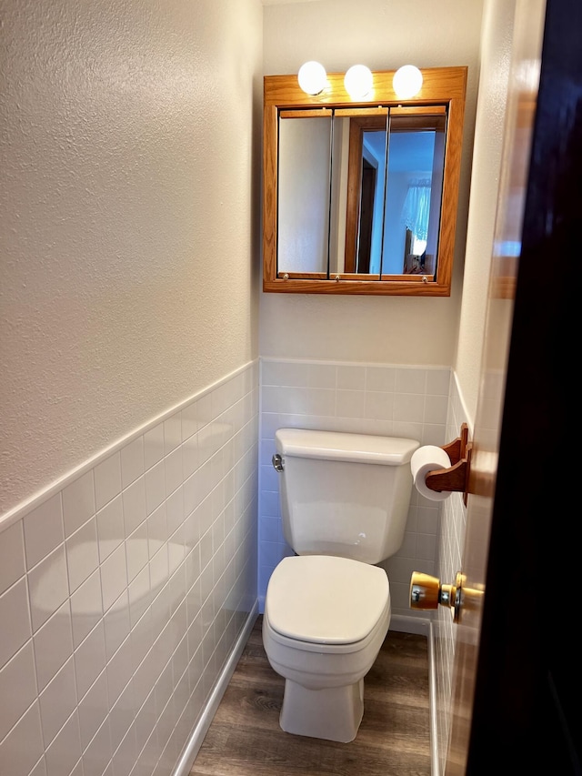 half bathroom with toilet, tile walls, wood finished floors, and wainscoting