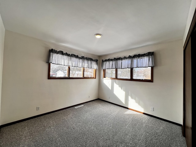 unfurnished room with carpet, visible vents, and baseboards