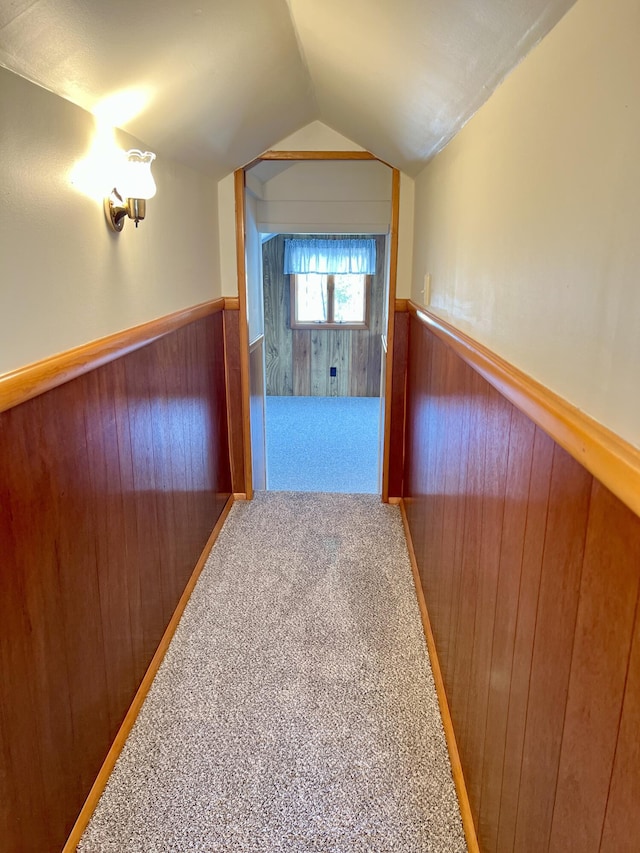 hall with carpet floors, a wainscoted wall, vaulted ceiling, and wooden walls