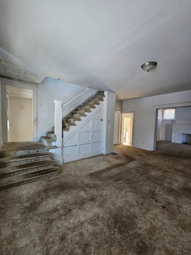 unfurnished living room featuring stairs and carpet