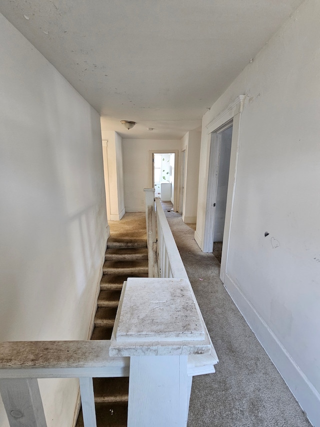 hallway featuring baseboards, dark colored carpet, and an upstairs landing