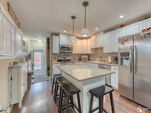 kitchen featuring stainless steel appliances, pendant lighting, white cabinets, and hardwood / wood-style flooring