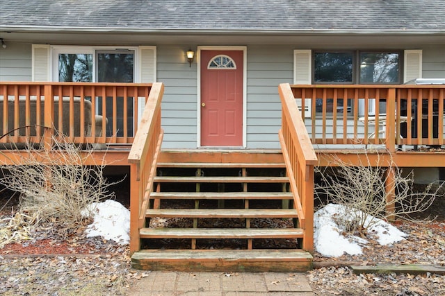 view of exterior entry featuring a shingled roof, central AC unit, and a deck