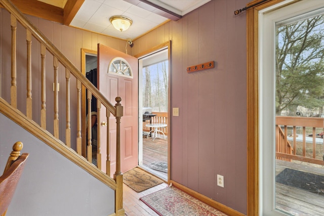 entryway featuring beamed ceiling, wood walls, stairway, and wood finished floors