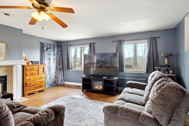 living area featuring ceiling fan, a fireplace, wood finished floors, and baseboards