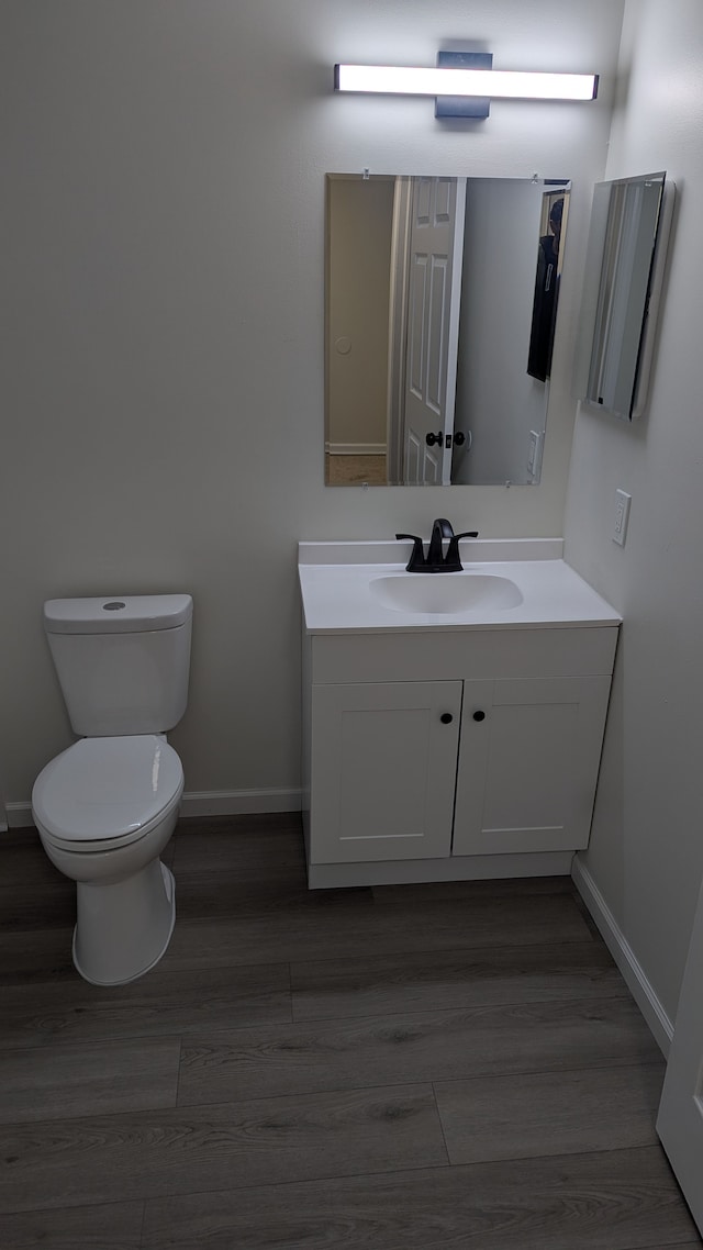 half bath featuring baseboards, vanity, toilet, and wood finished floors