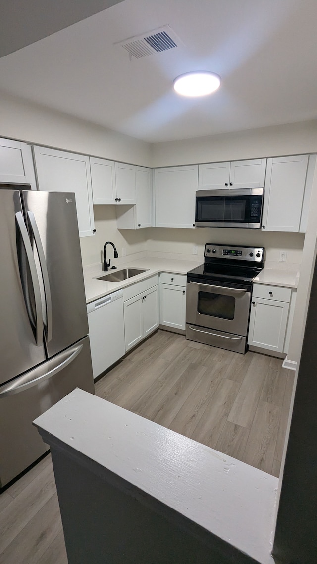 kitchen featuring stainless steel appliances, visible vents, white cabinetry, a sink, and light wood-type flooring