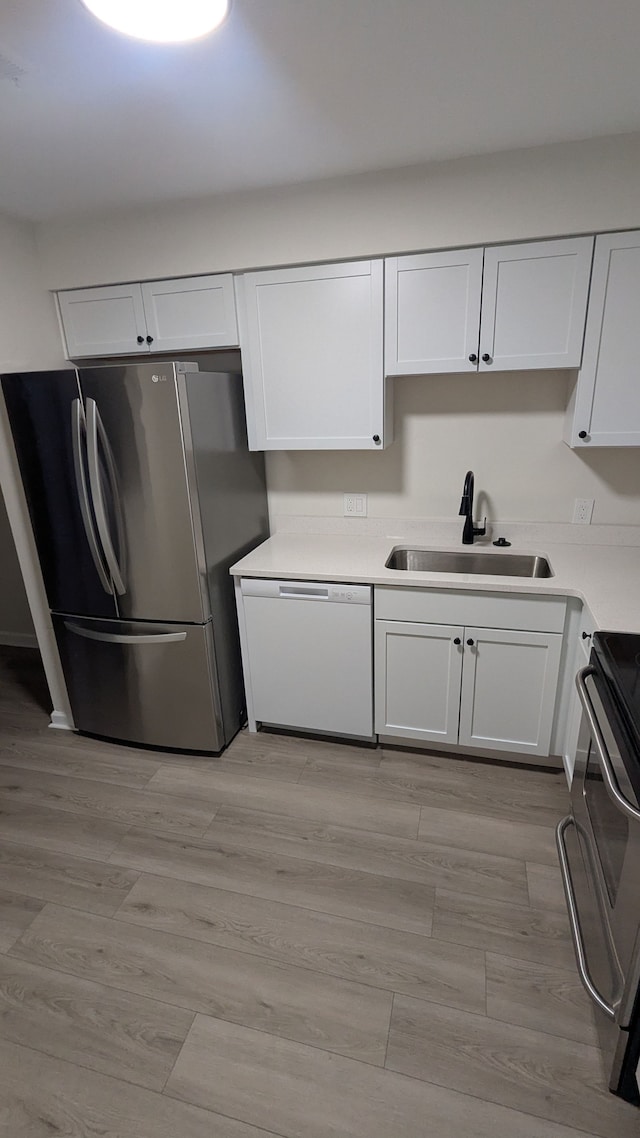 kitchen with white cabinets, dishwasher, stove, freestanding refrigerator, and a sink