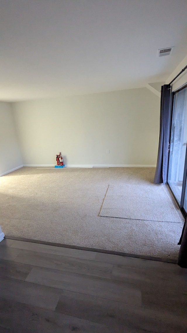 empty room with wood finished floors, carpet flooring, visible vents, and baseboards