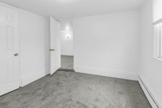 empty room with a baseboard heating unit, carpet, and baseboards
