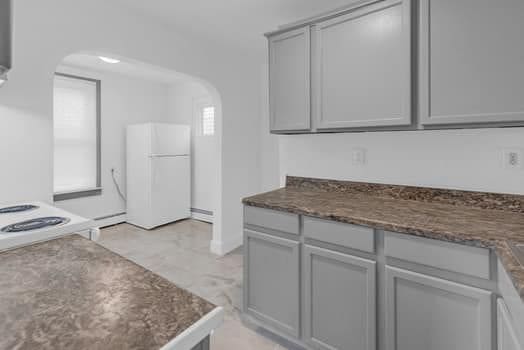 kitchen with arched walkways, dark stone counters, freestanding refrigerator, and gray cabinetry