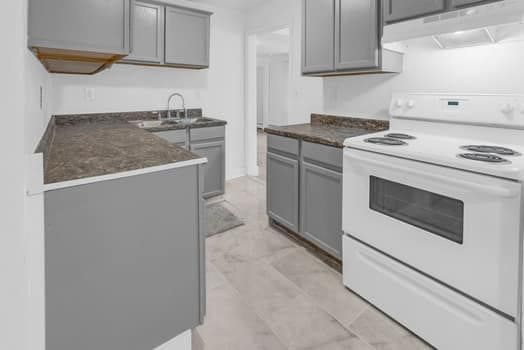 kitchen featuring dark countertops, gray cabinets, under cabinet range hood, and white range with electric cooktop