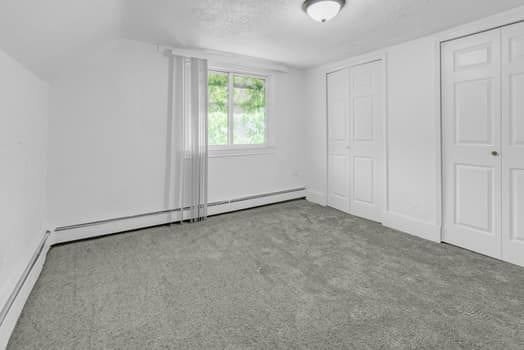 unfurnished bedroom featuring baseboard heating, carpet flooring, and two closets