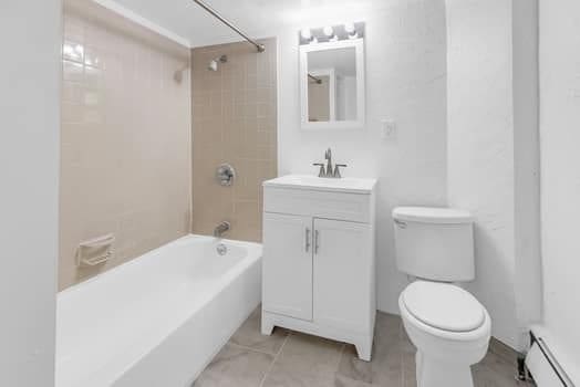 bathroom with a baseboard radiator, tile patterned flooring, toilet, vanity, and tub / shower combination