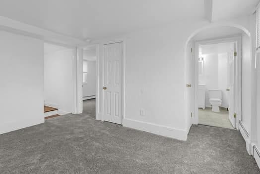 unfurnished bedroom featuring arched walkways, carpet floors, and a baseboard heating unit