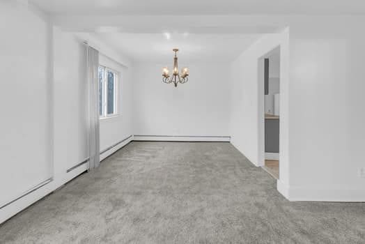 empty room featuring a chandelier, baseboard heating, and carpet