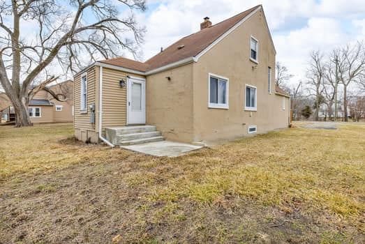 back of property with entry steps, a chimney, a lawn, and stucco siding
