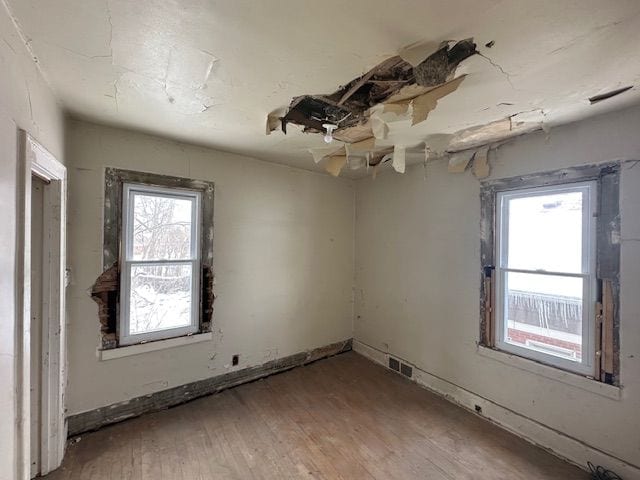 unfurnished room with wood-type flooring, visible vents, and baseboards