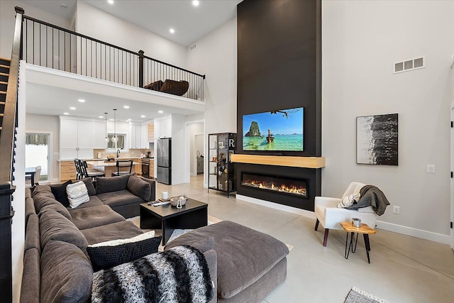 living area featuring baseboards, visible vents, a glass covered fireplace, a towering ceiling, and finished concrete floors