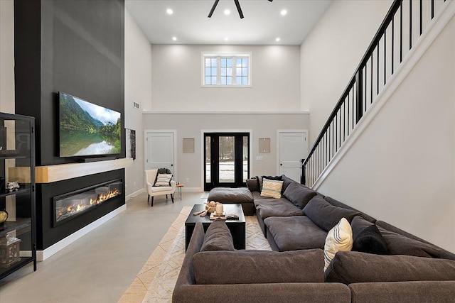 living room with baseboards, a glass covered fireplace, a high ceiling, stairs, and recessed lighting