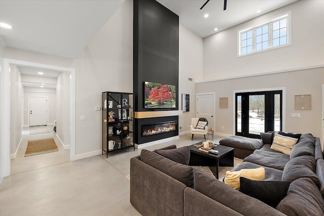 living area featuring recessed lighting, a high ceiling, finished concrete floors, a glass covered fireplace, and baseboards