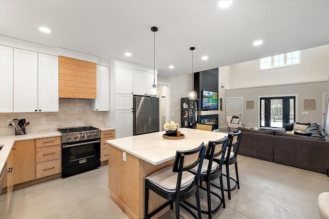 kitchen with finished concrete flooring, appliances with stainless steel finishes, a glass covered fireplace, and decorative backsplash