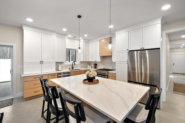 kitchen with tasteful backsplash, a breakfast bar, stainless steel appliances, concrete flooring, and a sink