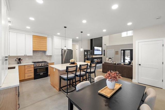 kitchen featuring concrete flooring, a glass covered fireplace, appliances with stainless steel finishes, decorative backsplash, and a kitchen bar