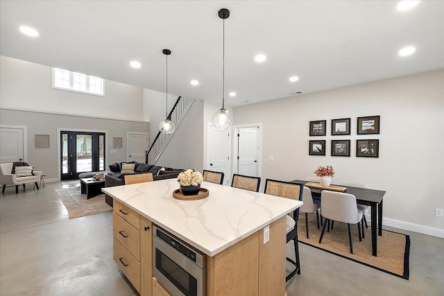 kitchen with a kitchen island, concrete floors, stainless steel microwave, and light brown cabinetry