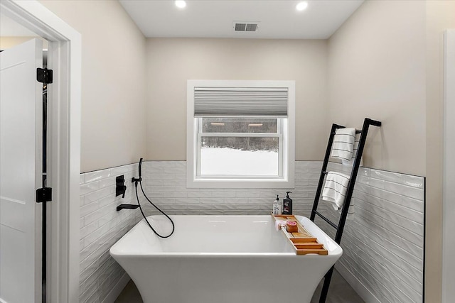 bathroom with a wainscoted wall, tile walls, recessed lighting, visible vents, and a freestanding bath