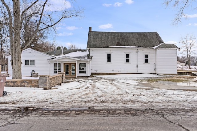 snow covered property with french doors and roof with shingles