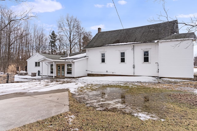 snow covered back of property featuring a porch and a chimney