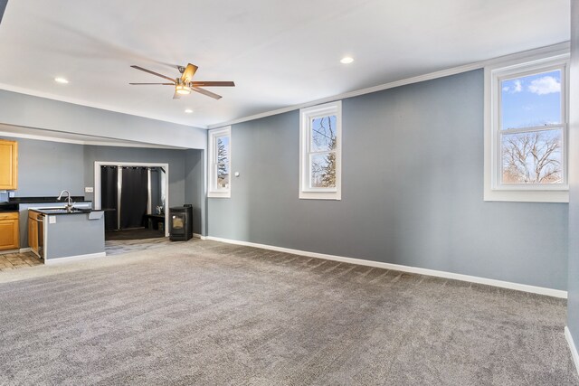 unfurnished living room with light carpet, baseboards, ceiling fan, ornamental molding, and a sink