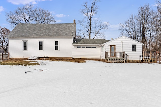 snow covered back of property featuring a chimney, roof with shingles, and a deck