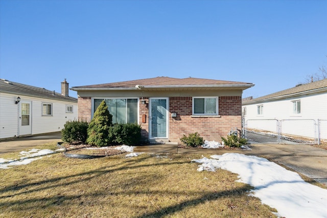 bungalow-style home featuring brick siding, a front lawn, fence, and a gate