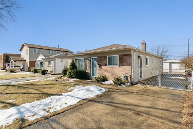 view of front of home featuring driveway, a chimney, a detached garage, a gate, and brick siding