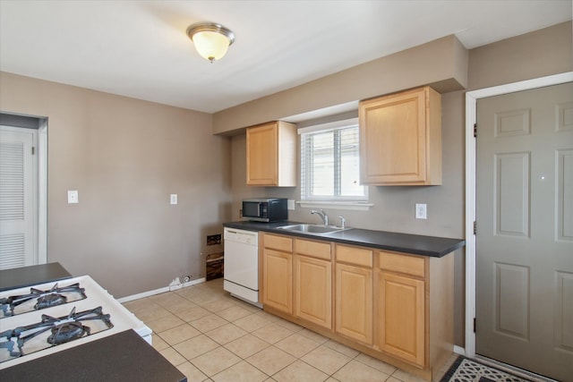 kitchen with light tile patterned floors, dark countertops, stainless steel microwave, white dishwasher, and a sink