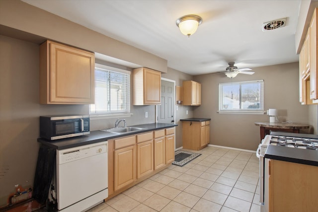 kitchen featuring white appliances, a sink, visible vents, light brown cabinetry, and dark countertops