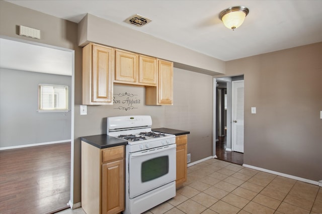 kitchen with white range with gas cooktop, visible vents, baseboards, dark countertops, and light brown cabinetry