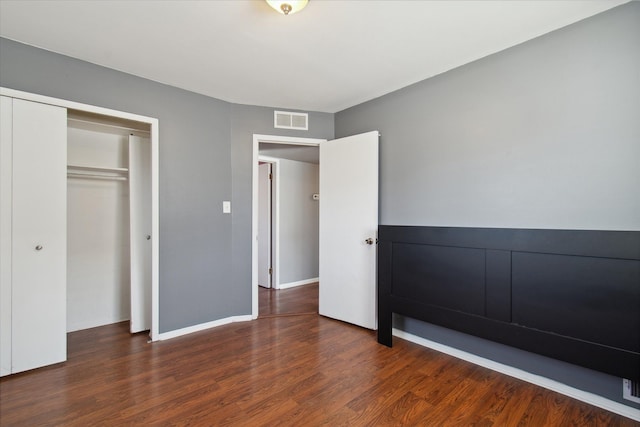 unfurnished bedroom with dark wood-style floors, baseboards, visible vents, and a closet