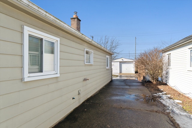 view of property exterior with driveway, a chimney, a detached garage, and an outbuilding