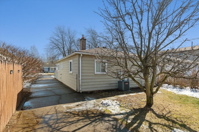 view of property exterior with a chimney, fence, and cooling unit